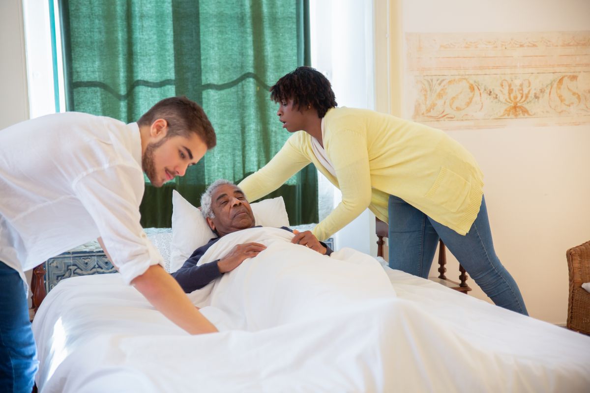 Two home health caregivers assisting elderly patient in bed at home