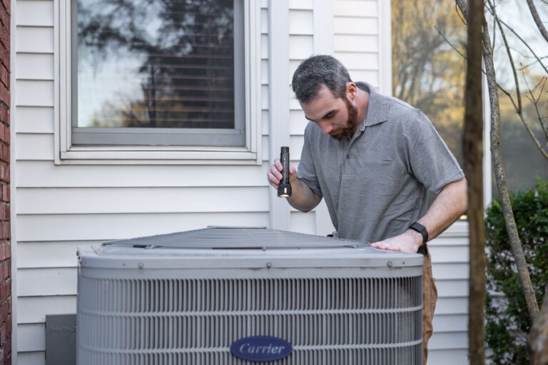 HVAC technician inspecting a residential outdoor air conditioning unit with a flashlight
