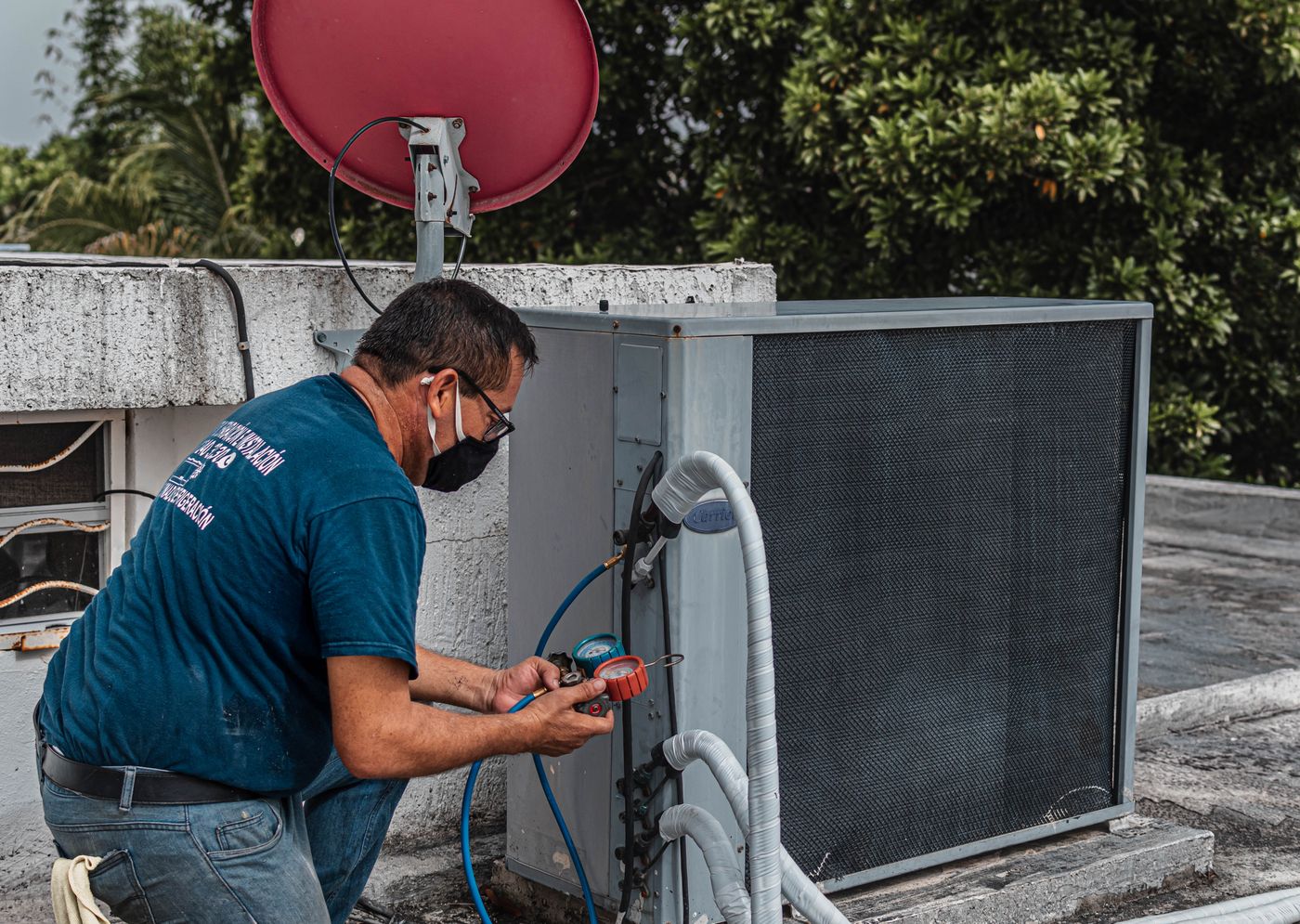 HVAC technician using gauges to repair an outdoor air conditioning unit during a service call