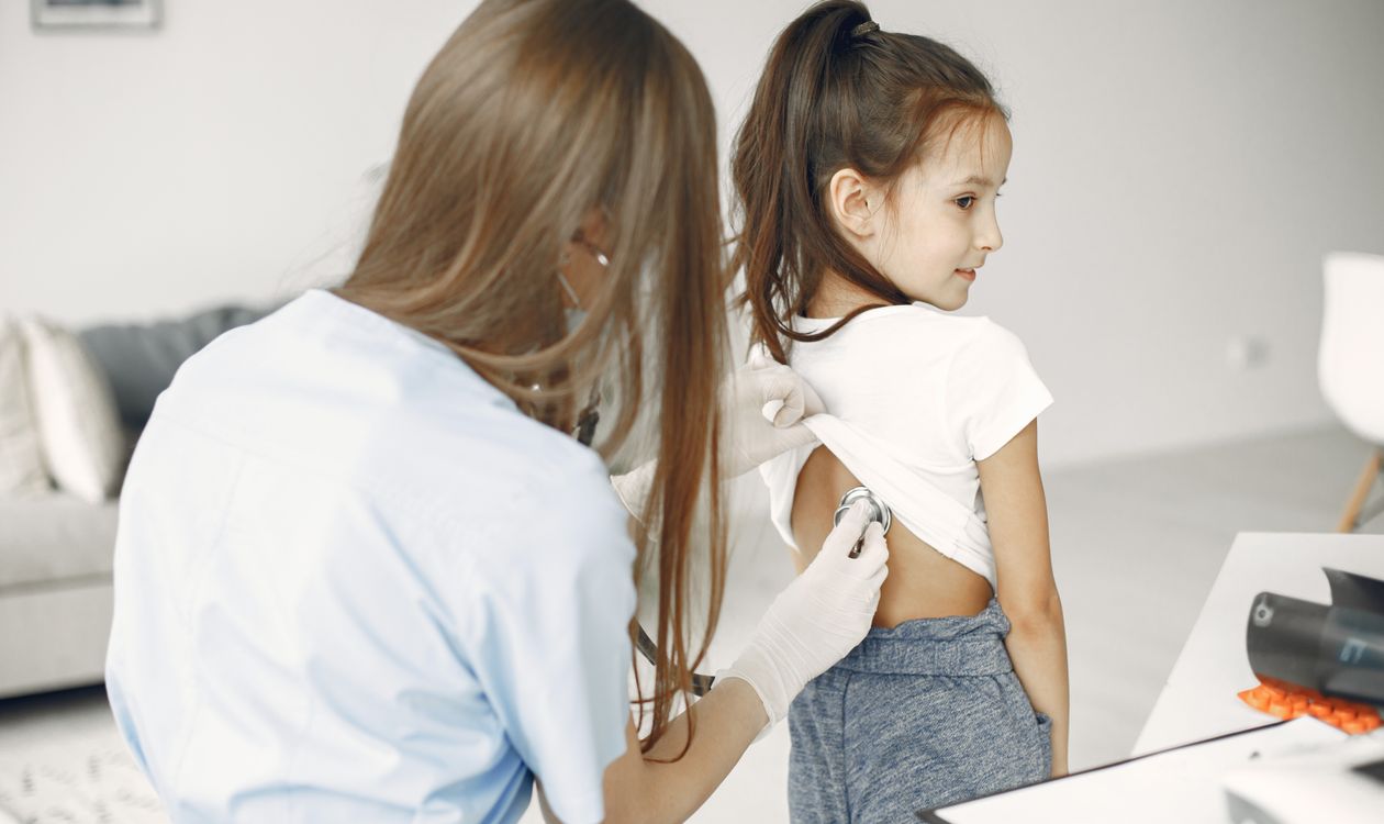 Doctor checking a young child's lungs with a stethoscope during a clinical exam