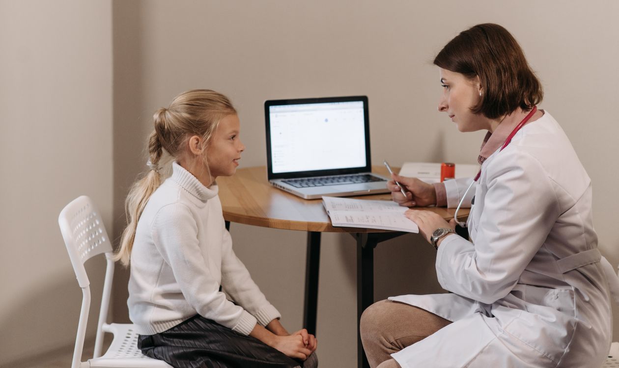 Pediatrician reviewing case notes on a laptop while consulting with a young patient