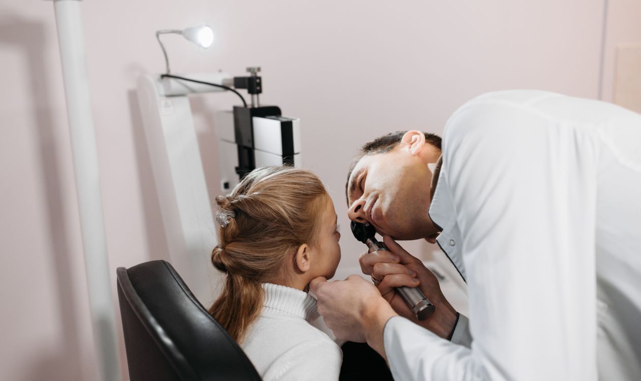 Doctor examining a young girl's ear with an otoscope during a pediatric appointment