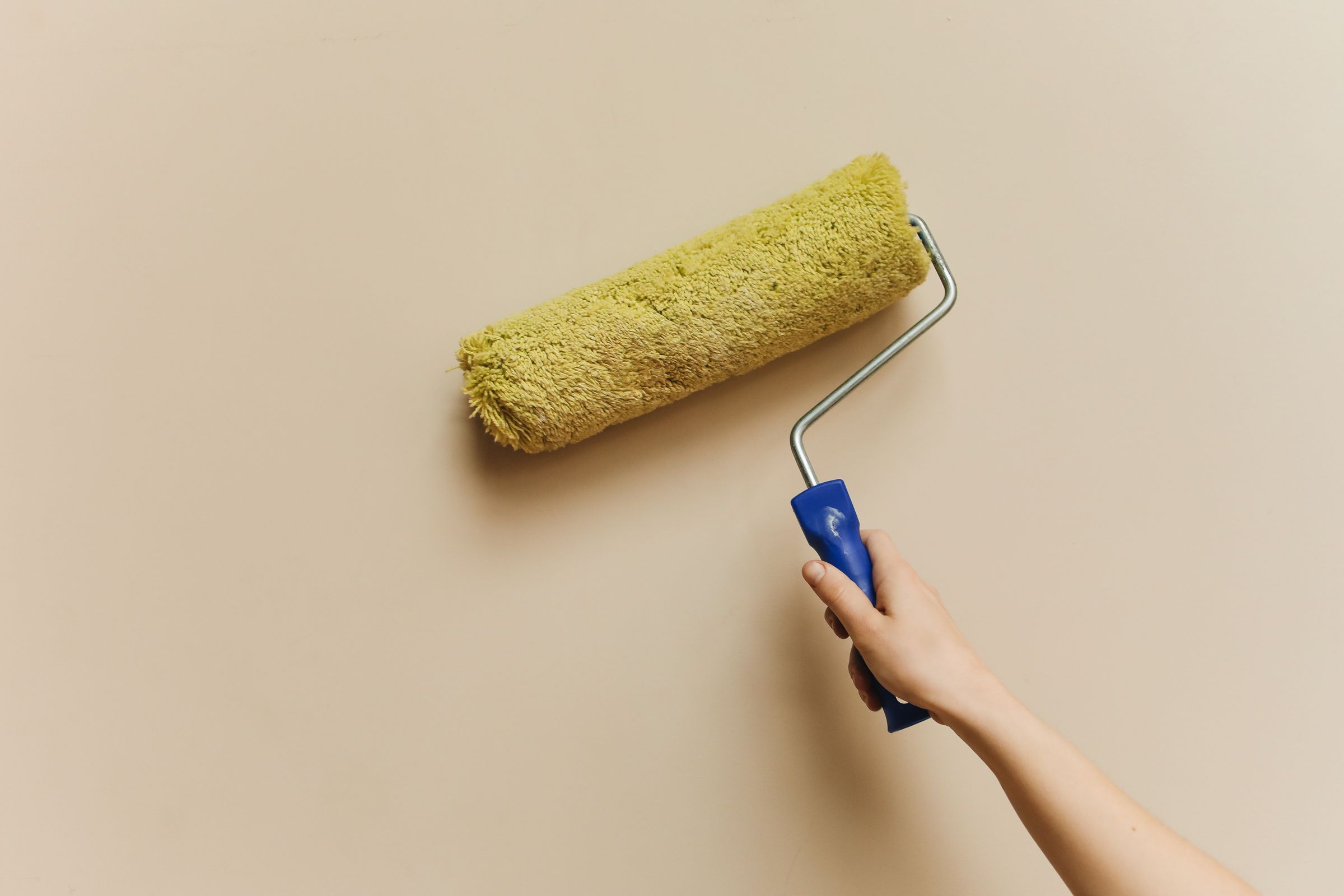 A painter's hand rolling a fresh coat of paint onto an interior wall with a roller