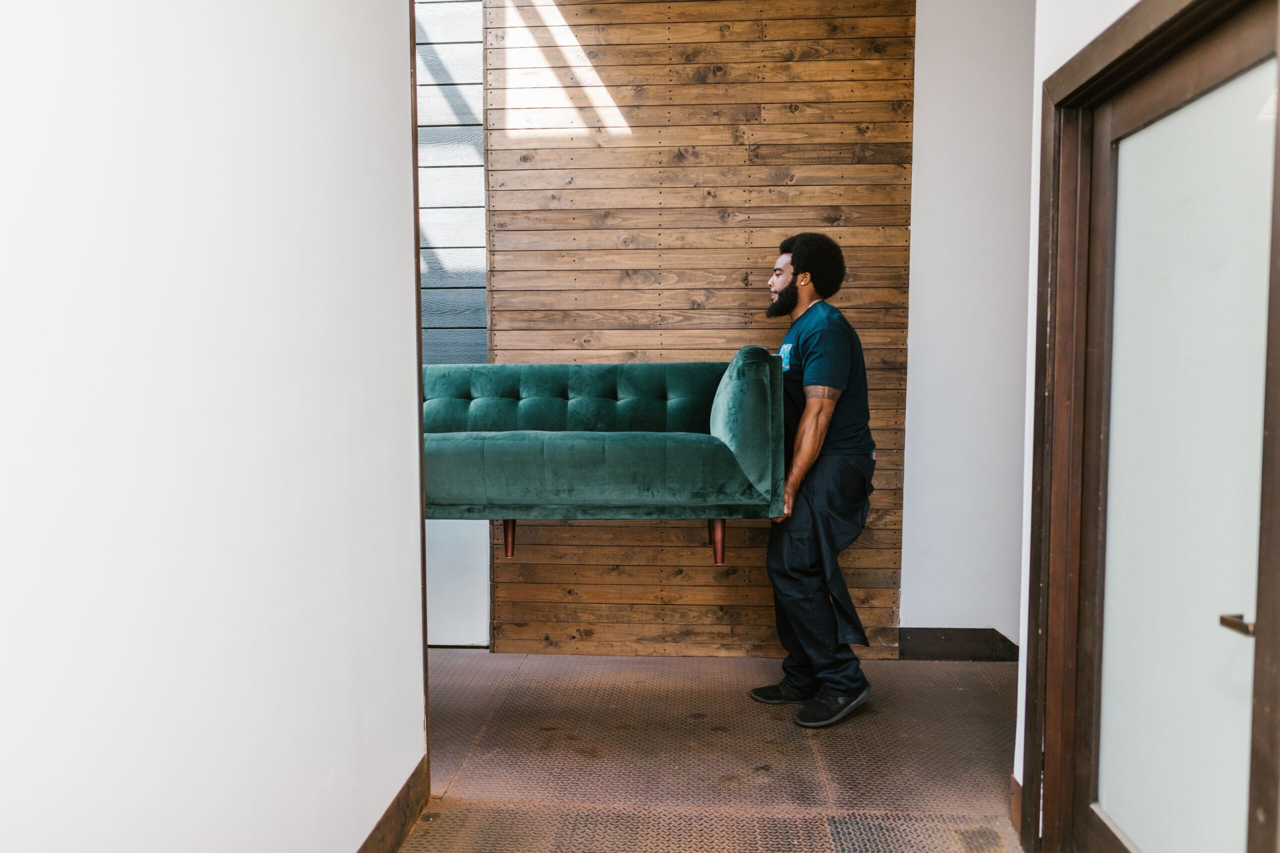 A junk removal worker in uniform carrying a couch out of a home