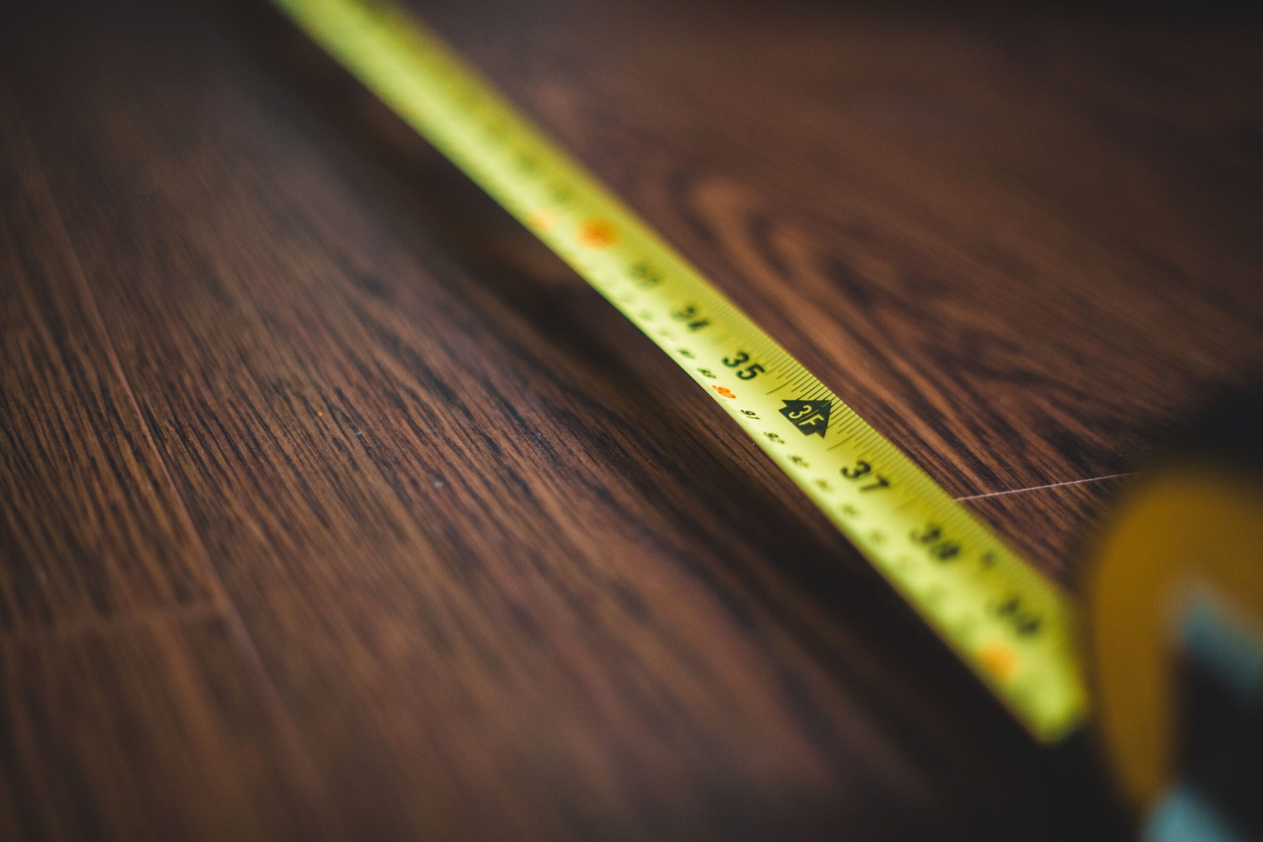 A yellow tape measure extended across a dark wood floor during a flooring estimate.