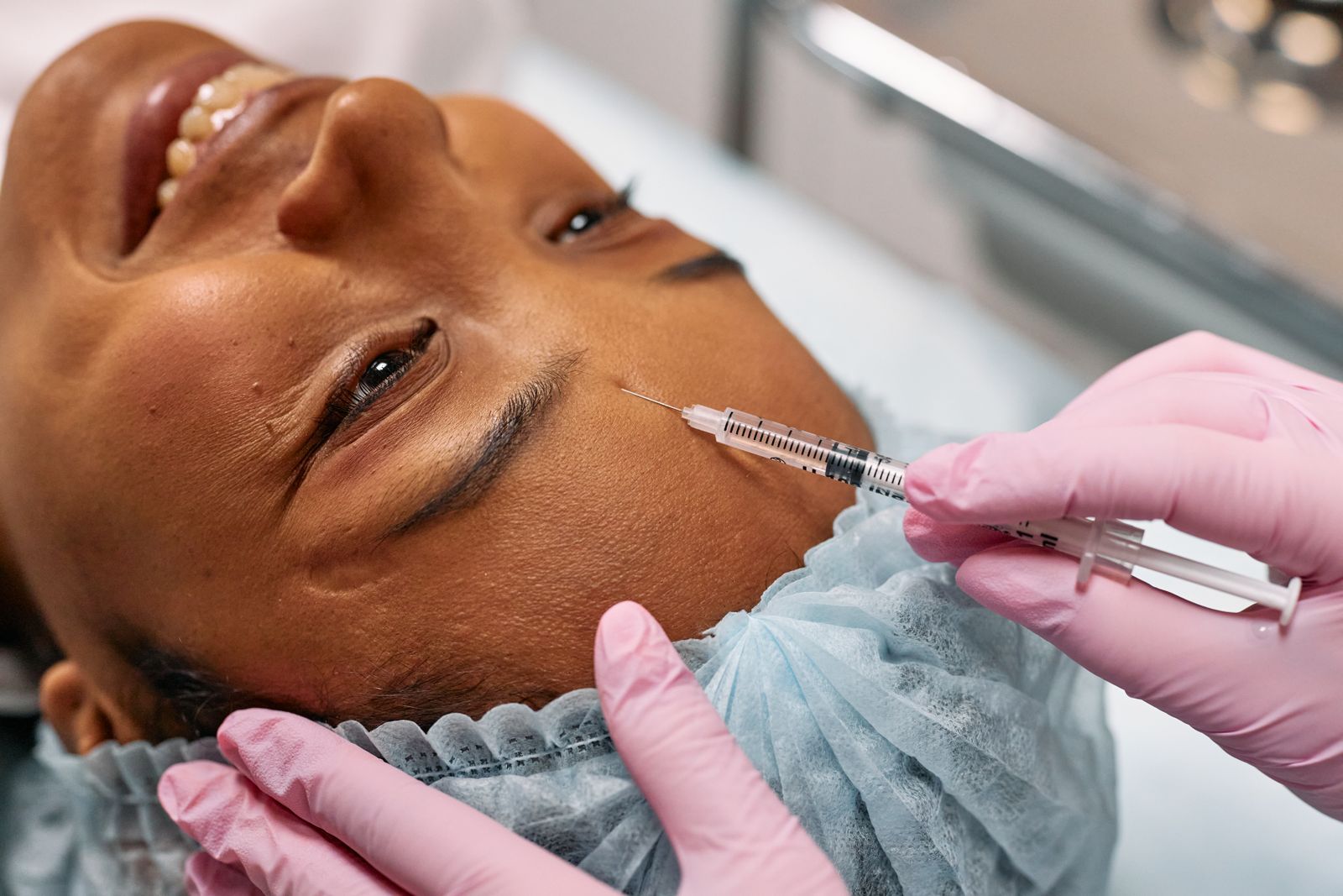 Aesthetic nurse in pink gloves administering a cosmetic injection near a client's eye