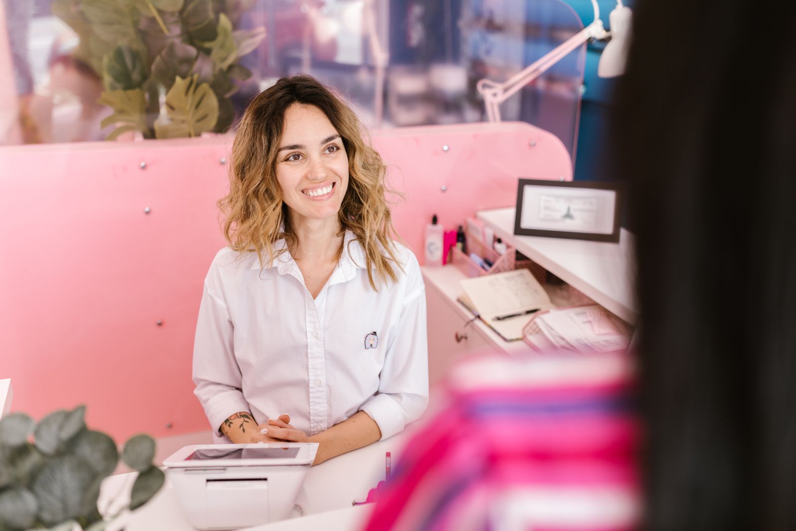 Smiling med spa receptionist in a white shirt greeting clients at a pink front desk