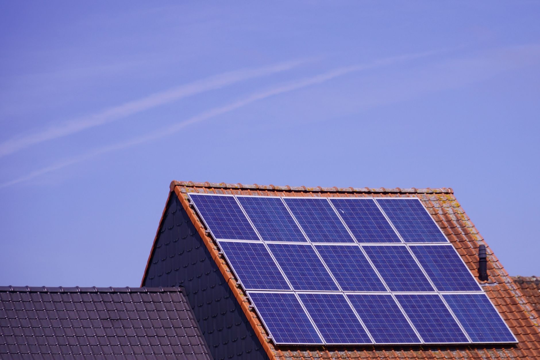 Residential rooftop solar panels mounted on a tiled roof against a clear blue sky