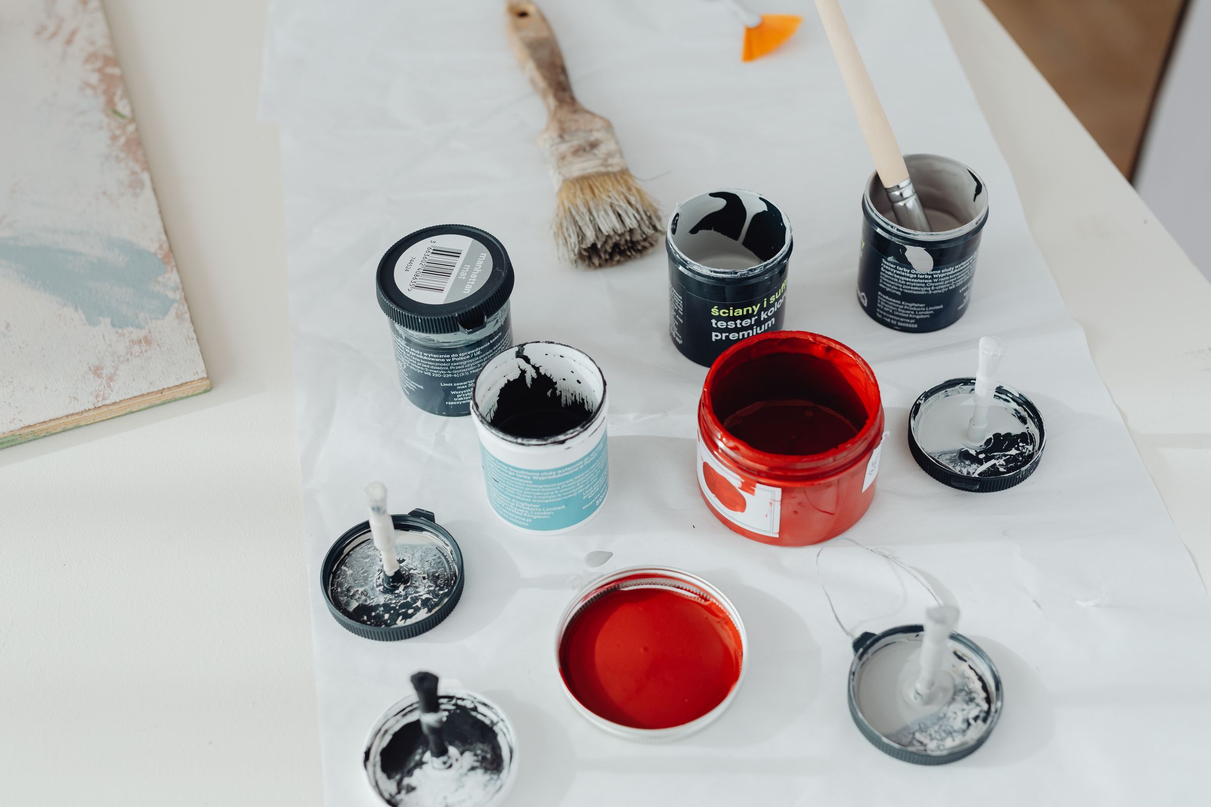 Open paint tester pots in red, grey and teal with a brush on a drop cloth