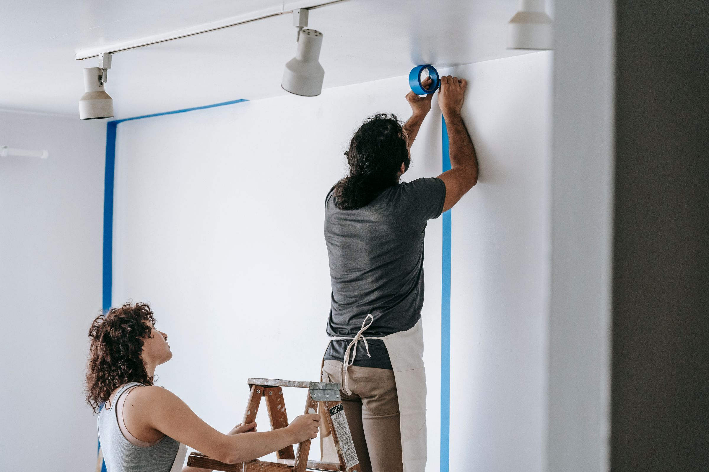 Two painters applying blue painter's tape to mask a wall before painting