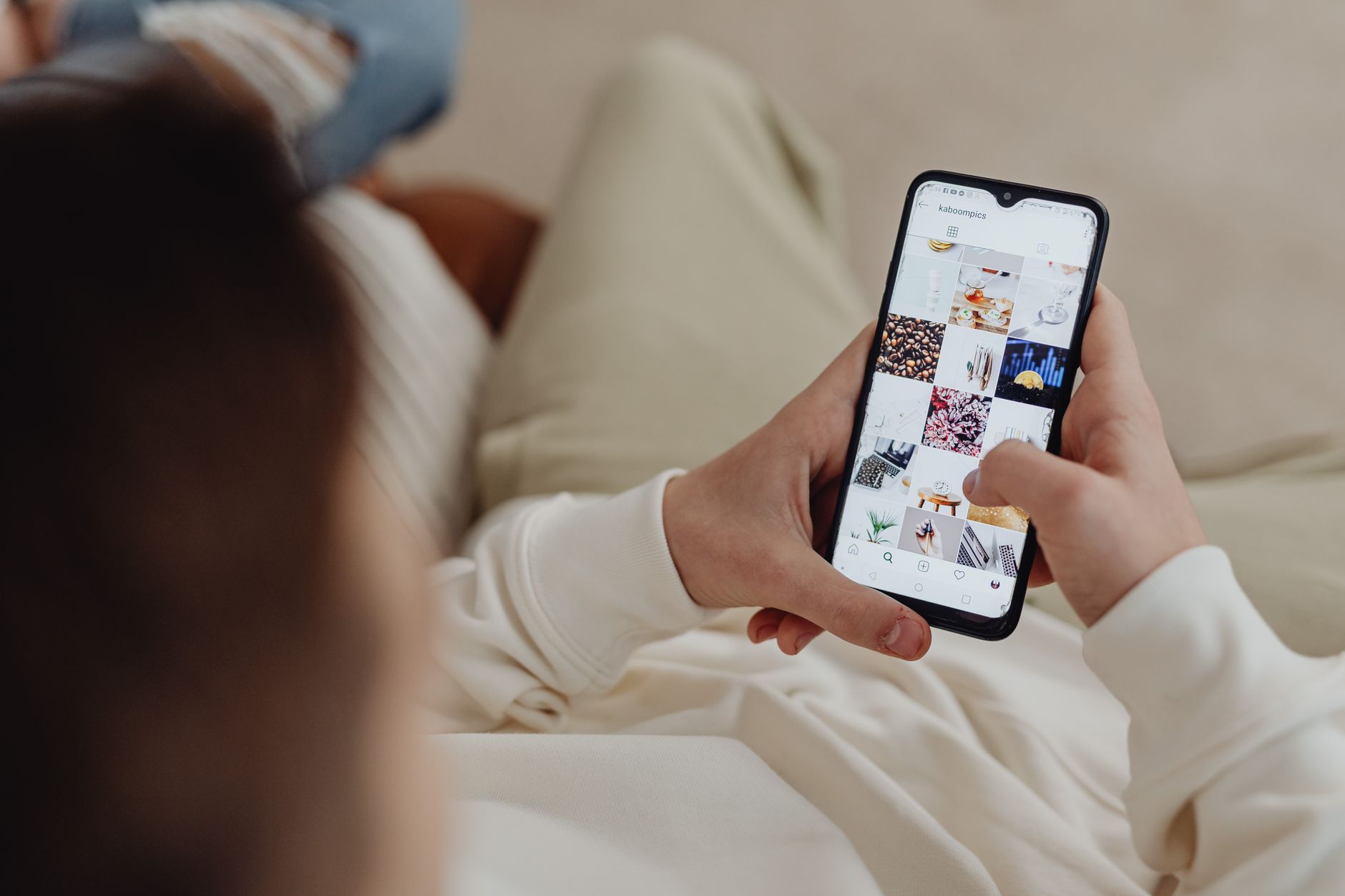 Person relaxing on a couch scrolling a social media feed on a phone