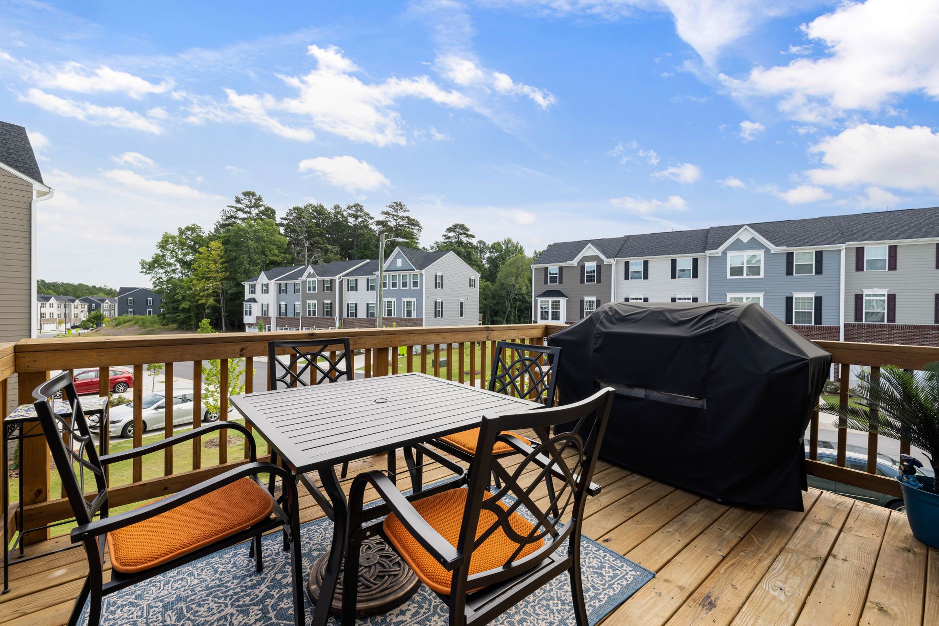 Residential wood deck with a gas grill and patio dining set overlooking a suburban neighborhood