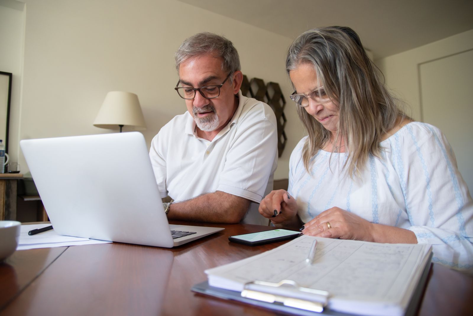 Retired couple reviewing financial documents and a laptop at their kitchen table