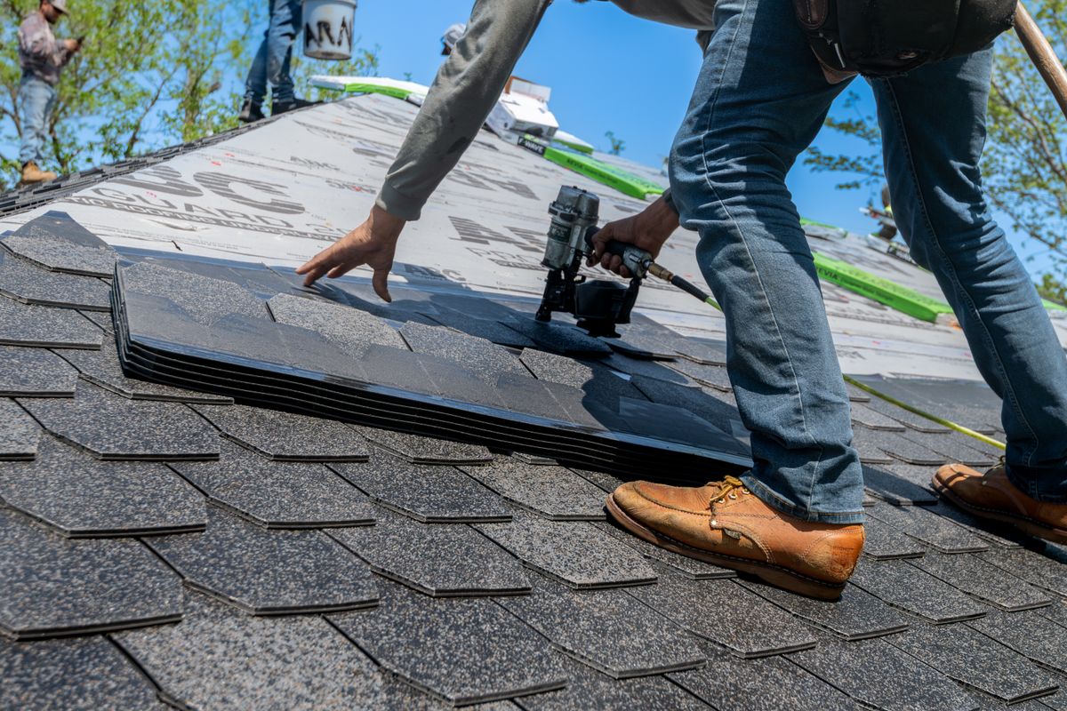 Roofer installing asphalt shingles with nail gun on residential roof