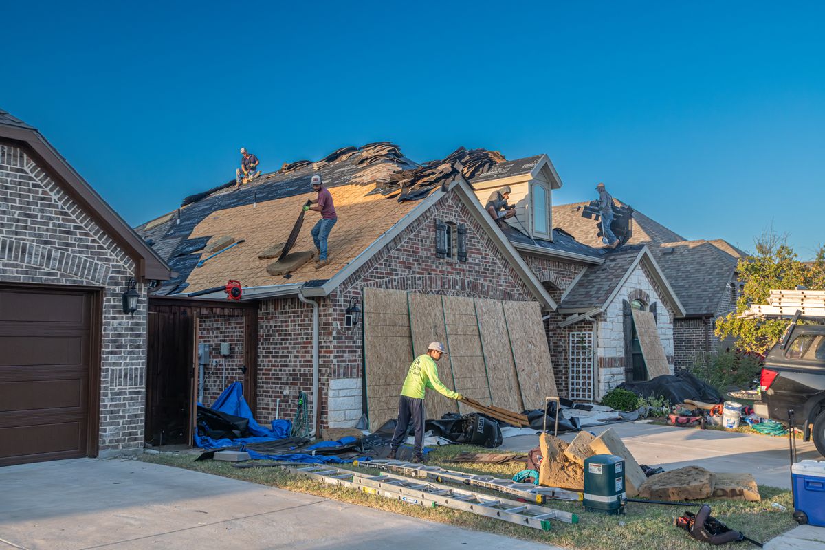 Crew tearing off and replacing shingles on a suburban home