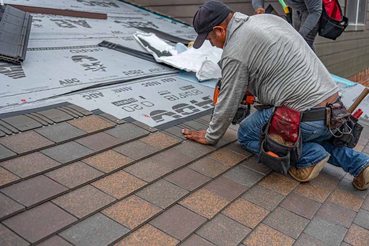 Roofer laying shingles over underlayment on a new roof install