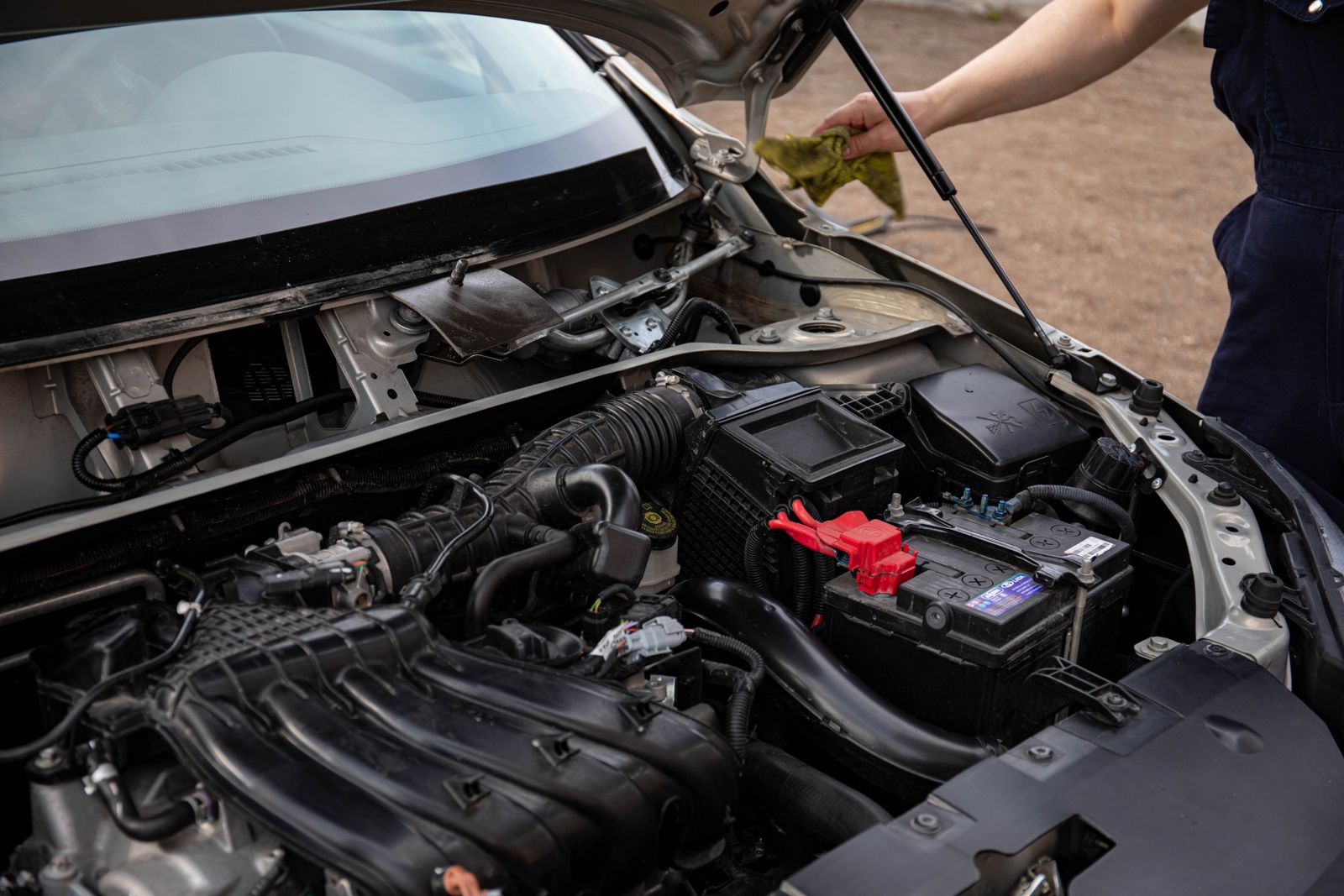 Mechanic inspecting the engine bay and battery of a car with the hood up