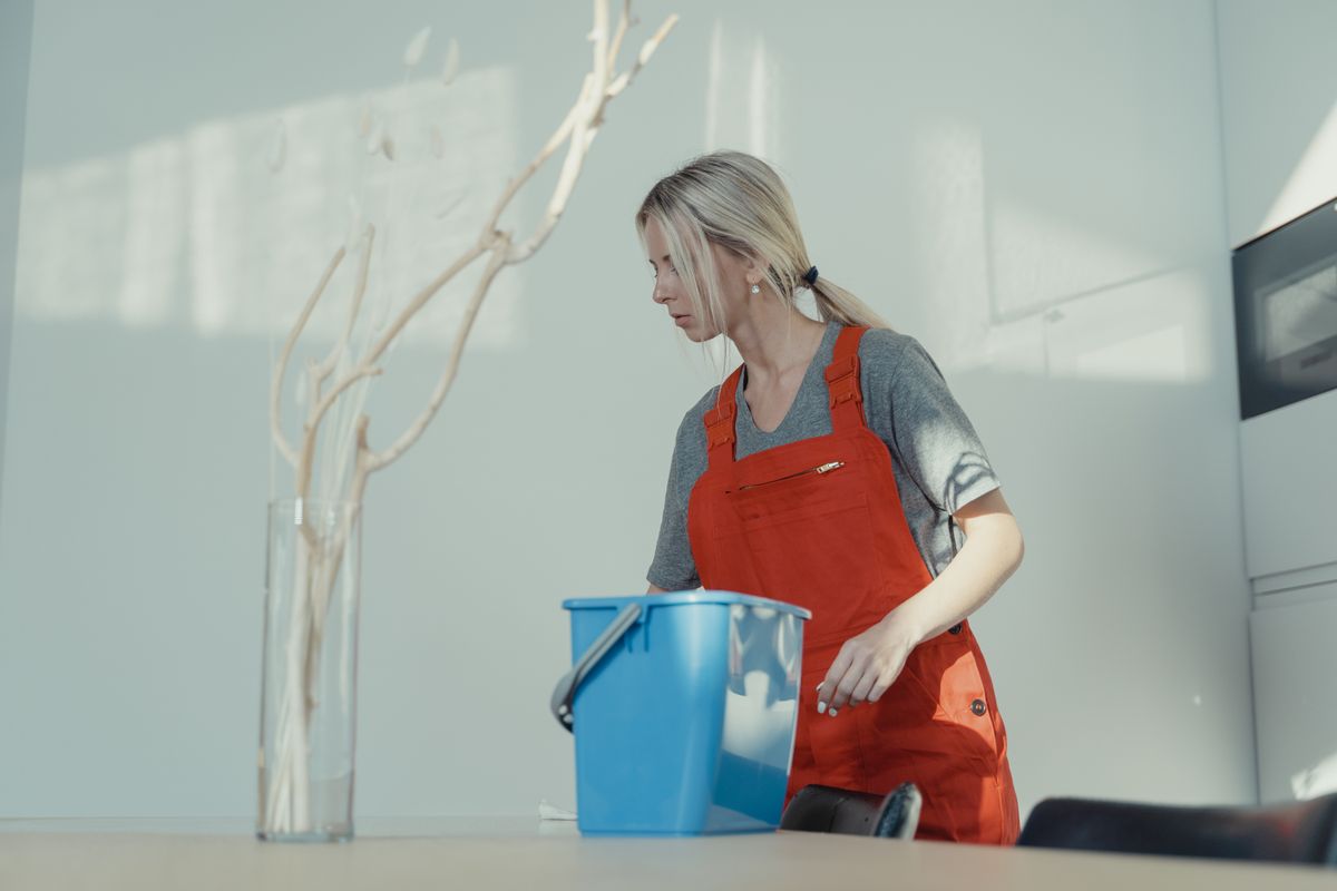 Professional cleaning technician in orange overalls preparing a bucket of supplies before a home cleaning job