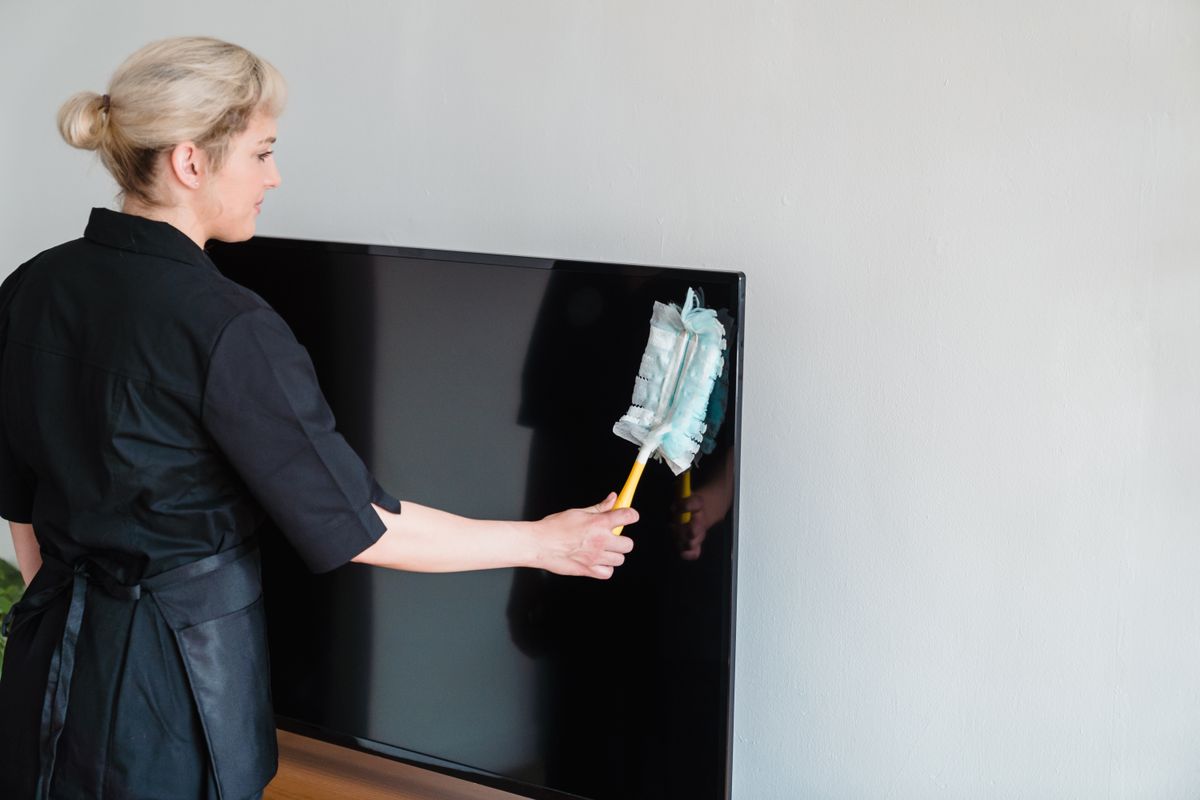 House cleaner dusting a television screen during a residential cleaning appointment