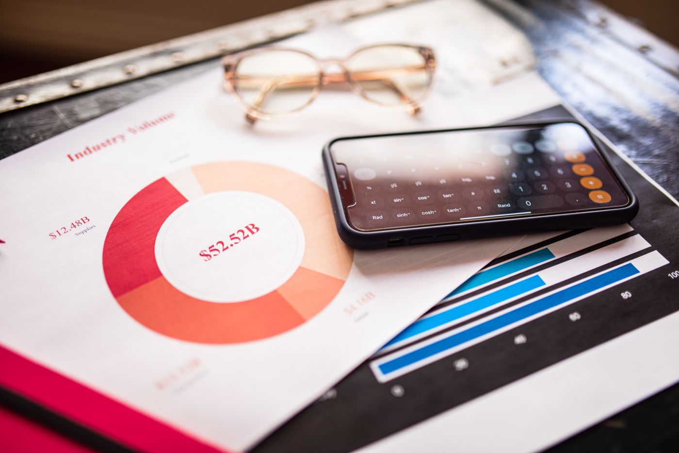 Printed charts, a calculator app on a phone, and reading glasses on a desk representing SEO return on investment