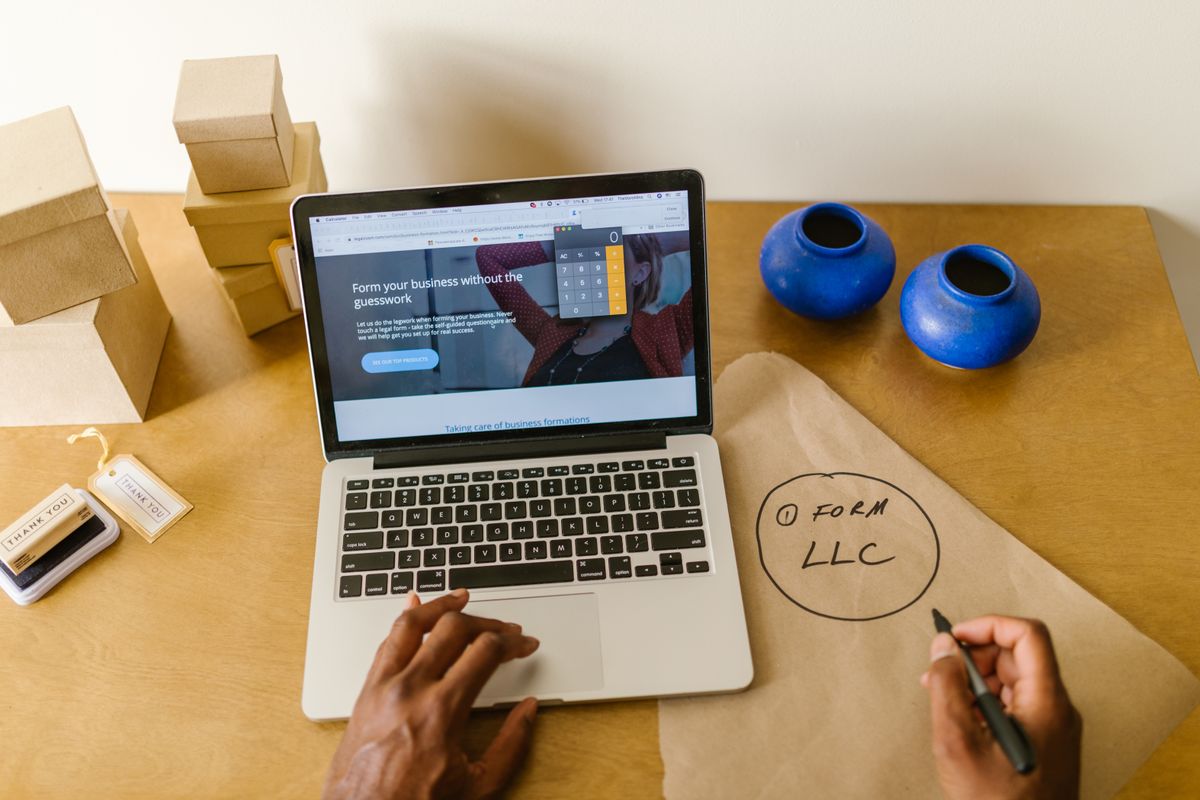 A small business owner managing online orders and packaging at a desk with a laptop