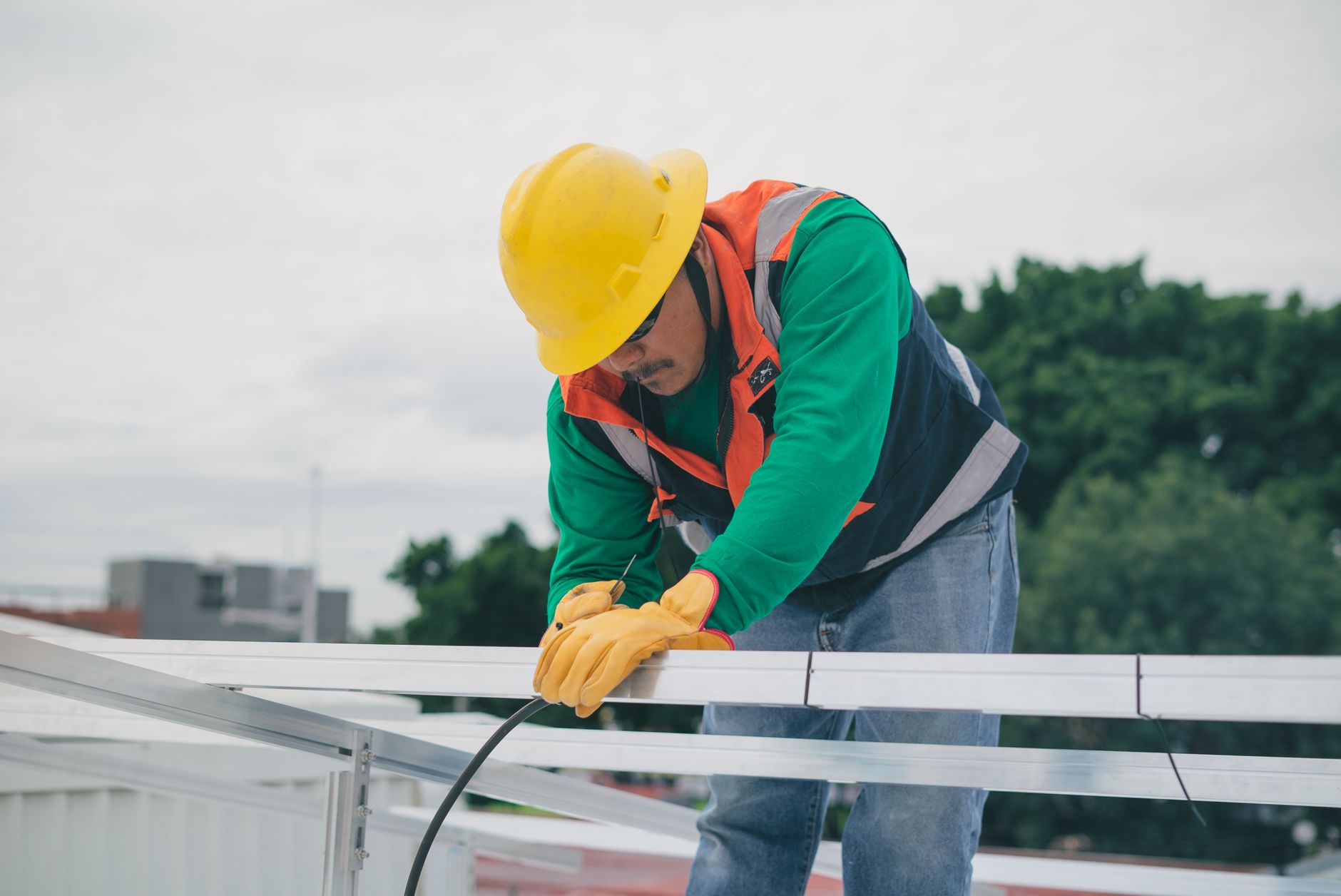 A solar technician in a yellow hard hat securing aluminum panel mounting rails on a rooftop