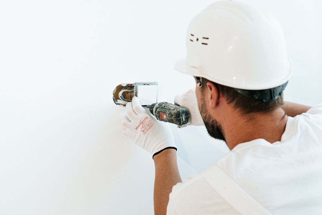 Contractor in a hard hat drilling into a wall during a home repair project