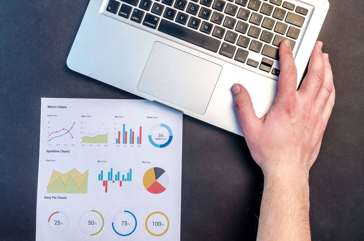 Hand resting on a laptop keyboard beside printed analytics charts showing bar graphs and pie charts
