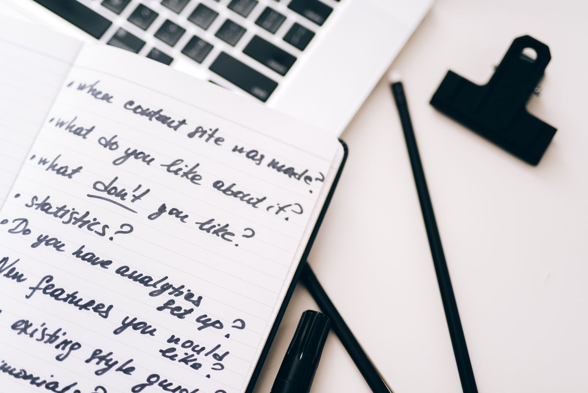 Handwritten content planning questions in notepad beside laptop for blog research