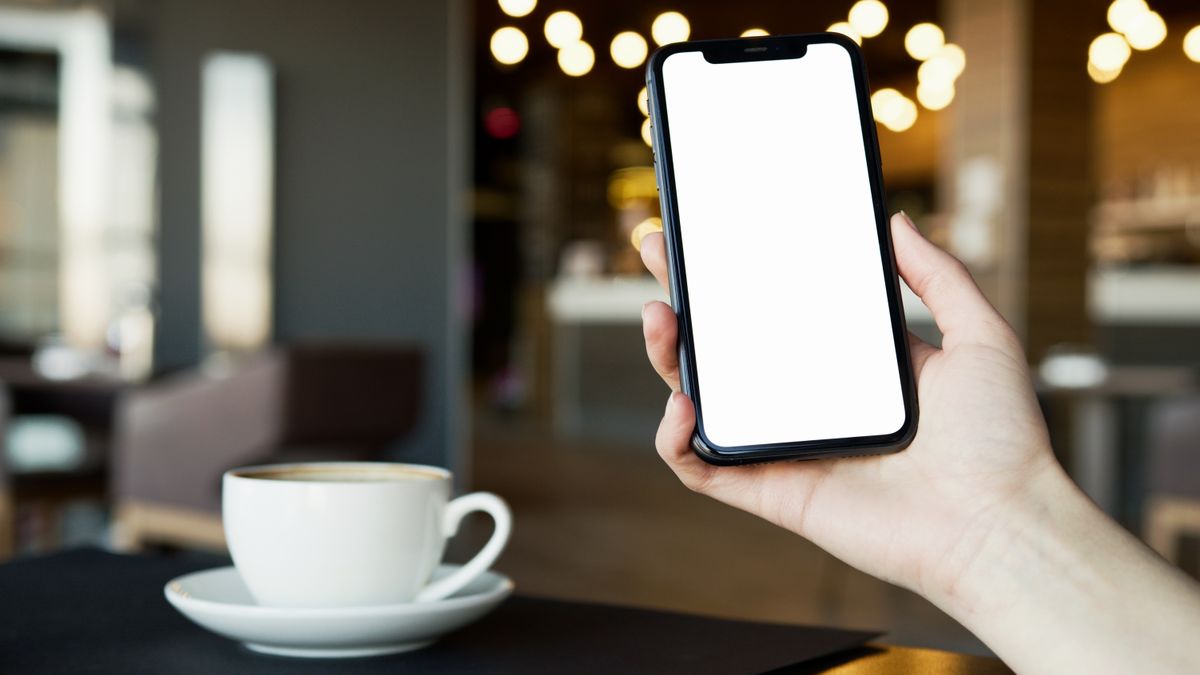 Person holding a smartphone in a coffee shop, ready to search for a local business