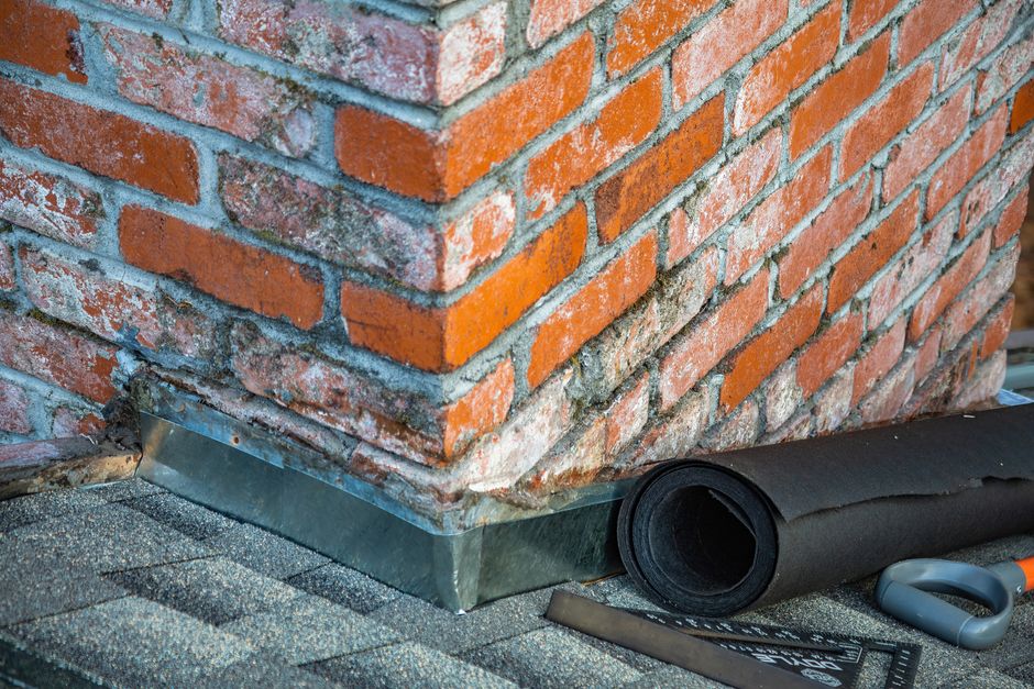 Close-up of a technician repairing brick chimney flashing on a roof