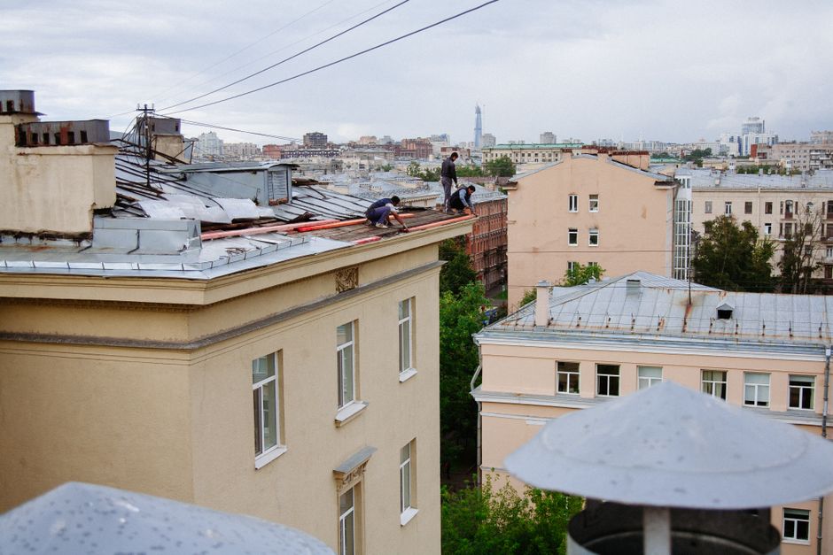Roofing and chimney technicians working on a rooftop above a city skyline