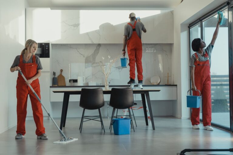 Group of commercial cleaners in red uniforms cleaning a glass office building interior