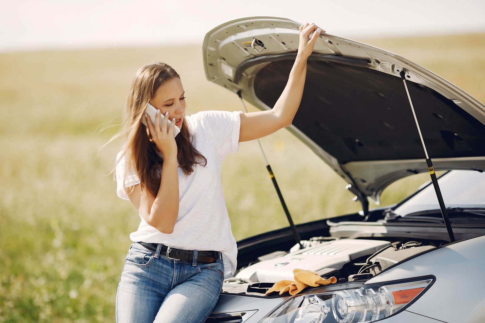Stranded driver calling for roadside help next to a broken-down car