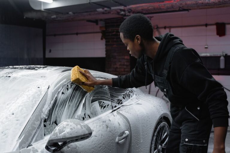Detailer hand-washing a car with a sponge in a professional detailing bay