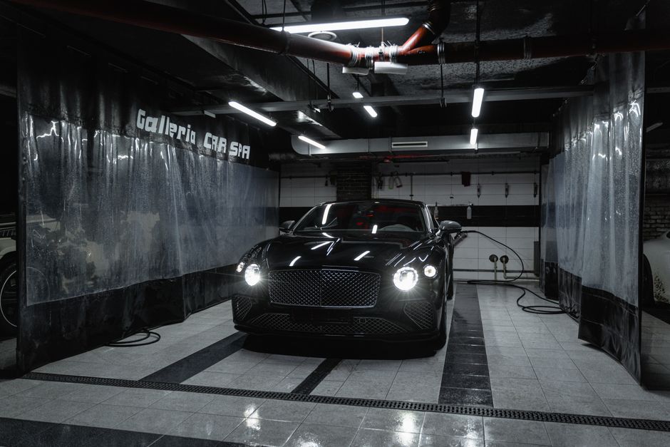 Black luxury car parked inside a premium detailing bay with overhead lighting