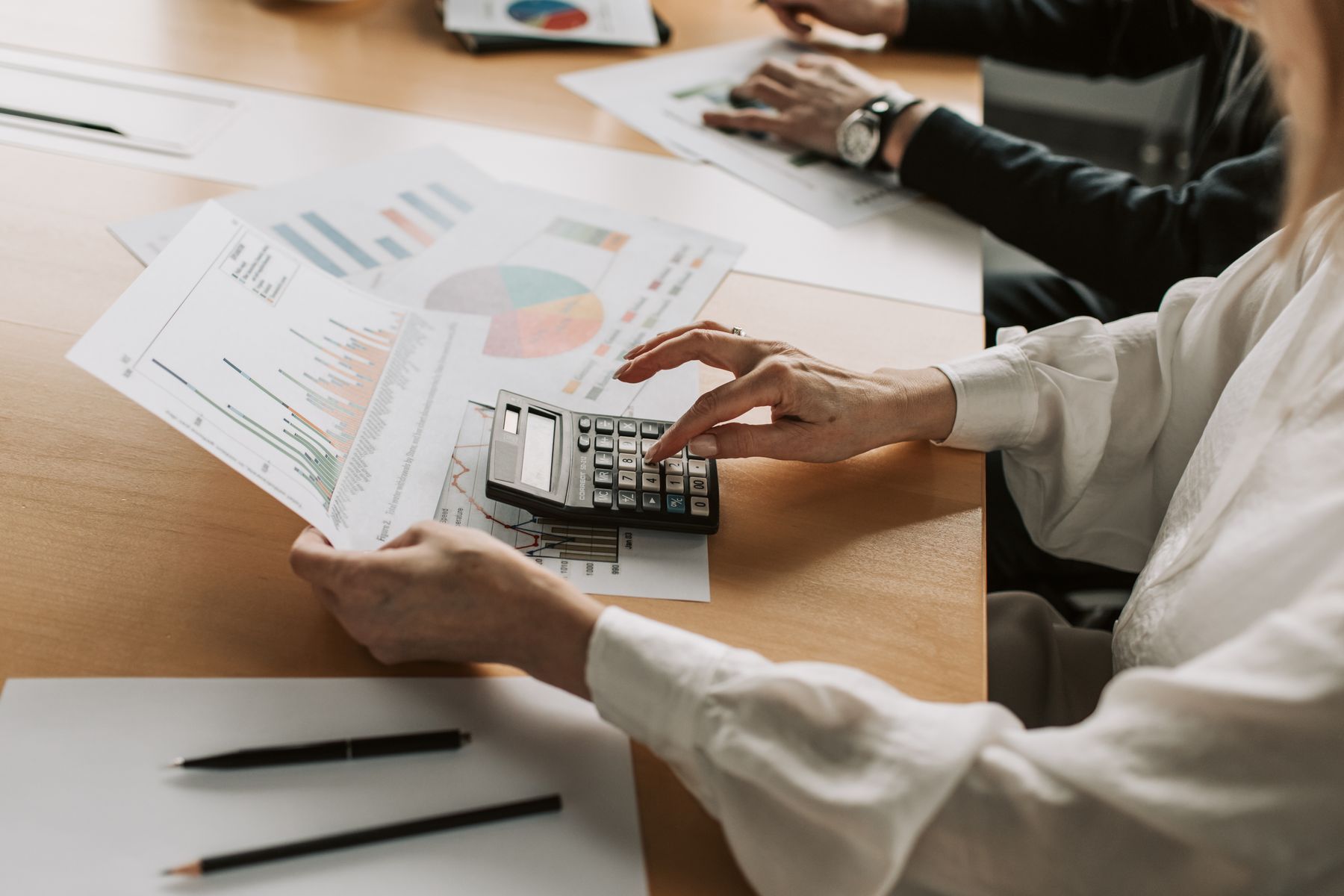 Hands calculating marketing budget numbers with a calculator and charts