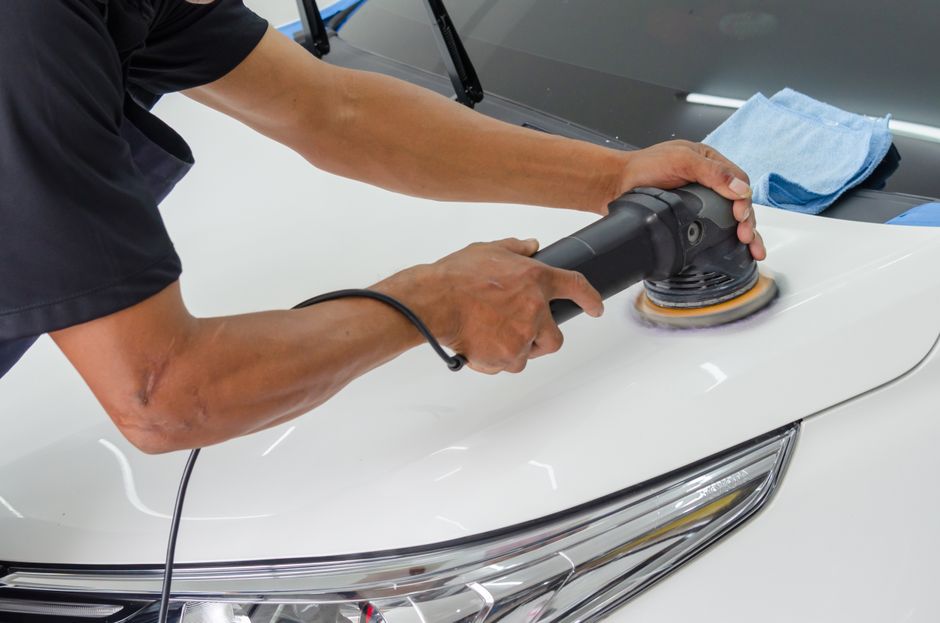 Detailer using an orbital polisher to correct paint on a white car