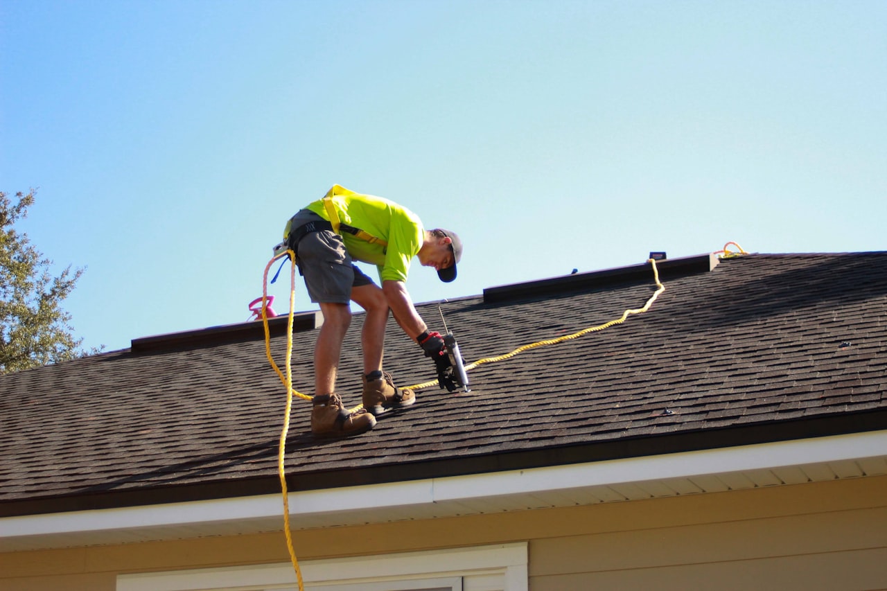roofer with power tools working on roof shingles