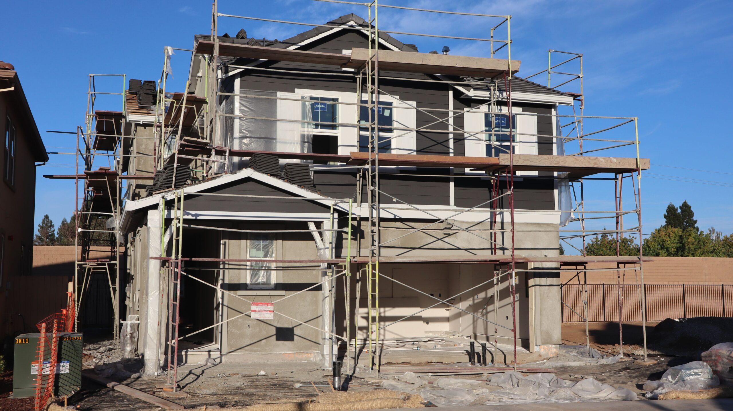 Two-story house under scaffolding during a siding replacement project