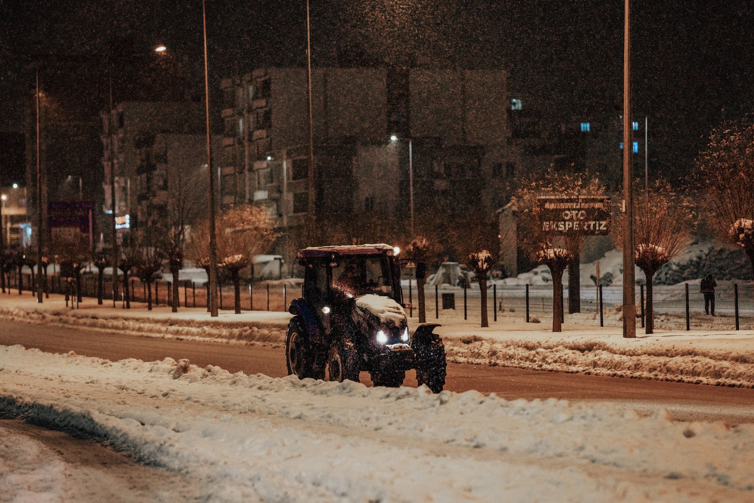 Snow plow truck clearing a city street at night during a storm