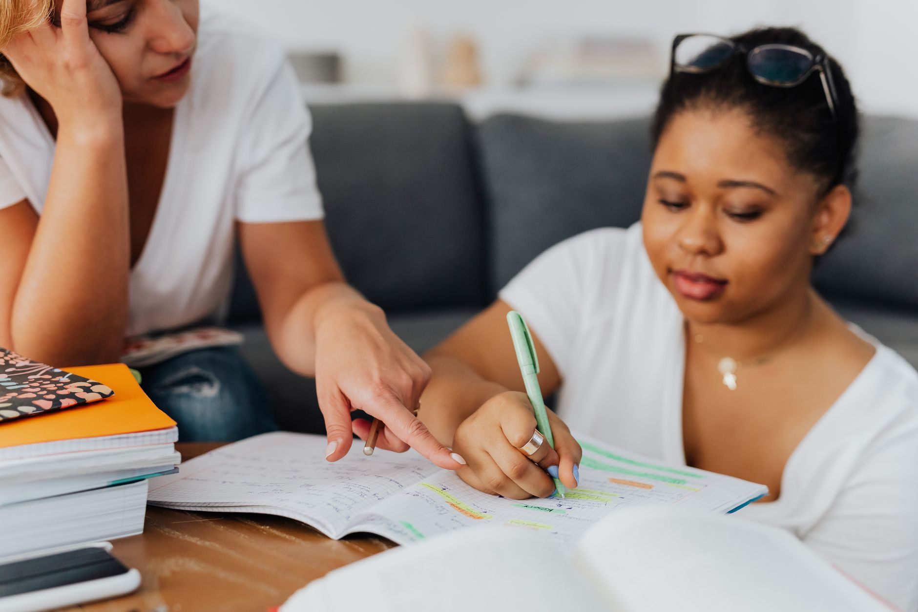 Adult tutor explaining a lesson to a student at a table with books and papers