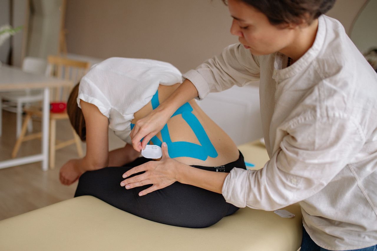 Physical therapist applying kinesiology tape to a patient's lower back during a pain treatment session