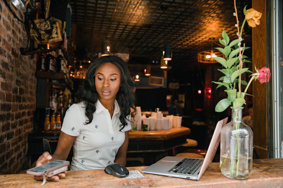 Small business owner checking her phone and laptop at the counter of her shop