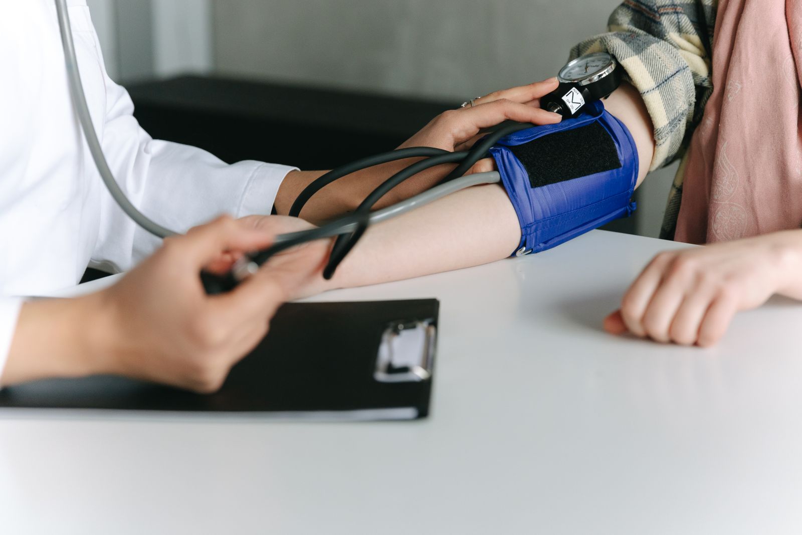 Doctor checking a patient's blood pressure with a manual cuff and stethoscope during a consultation