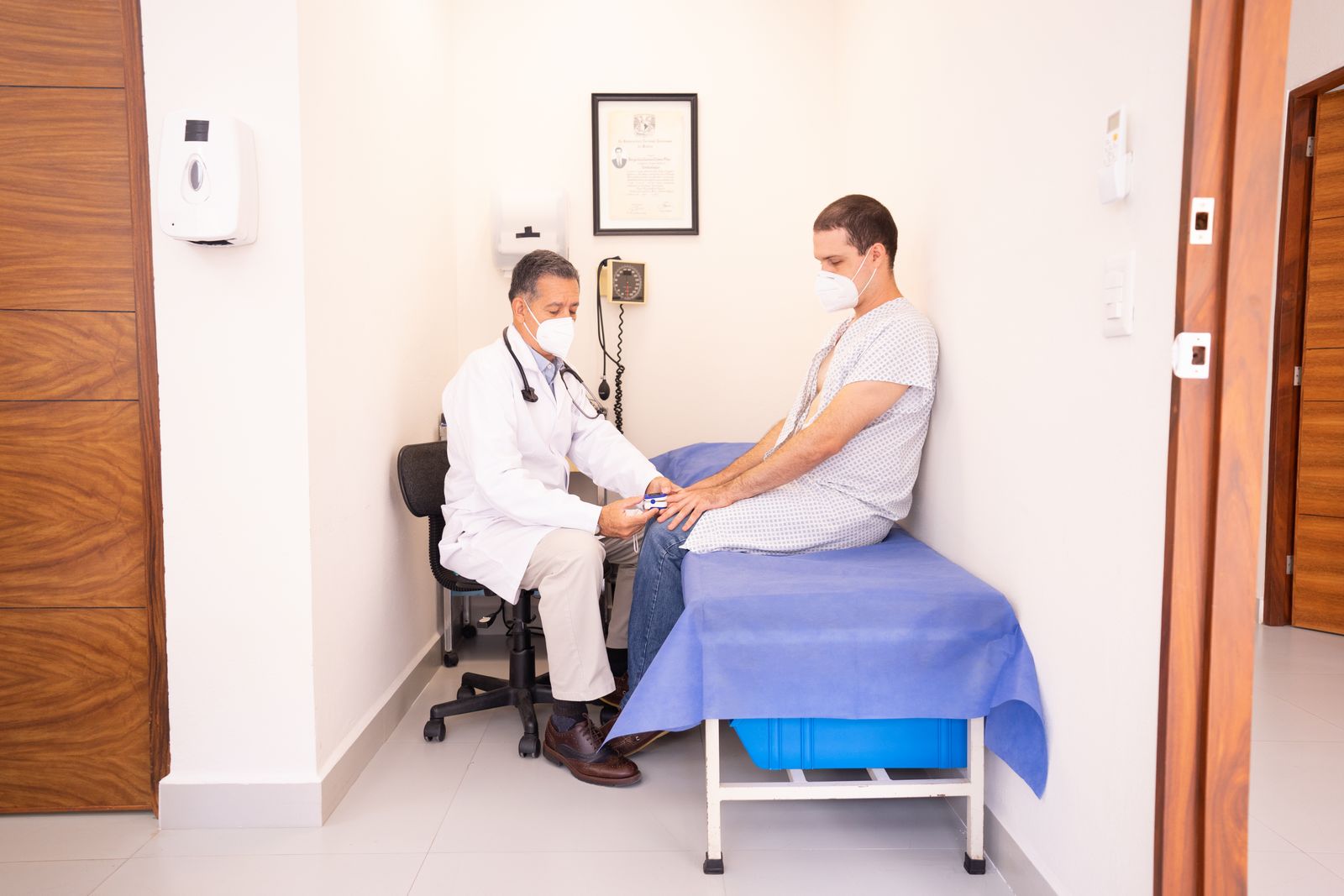 Doctor checking a seated patient's pulse oximeter reading in a small exam room