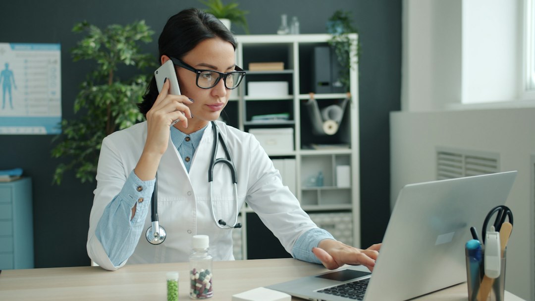 Doctor using a laptop and phone at her desk in a clinic office