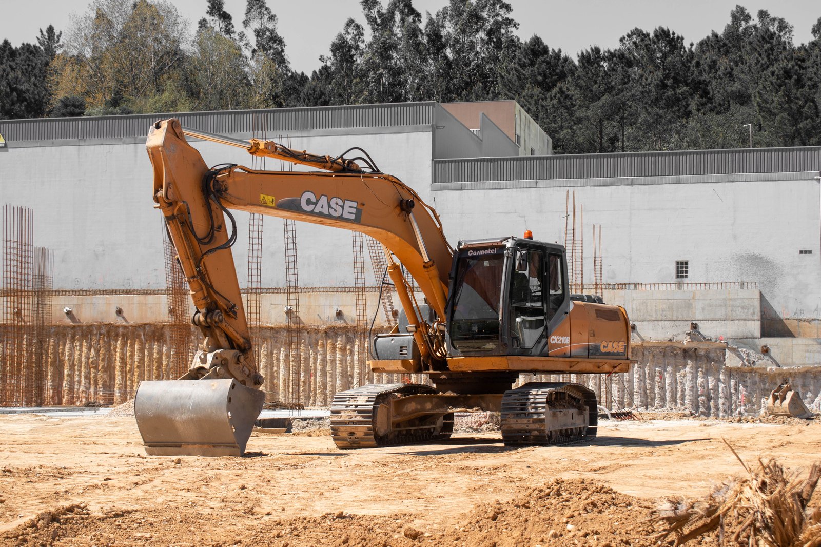 Excavator digging a foundation trench at a commercial construction site with rebar forms visible