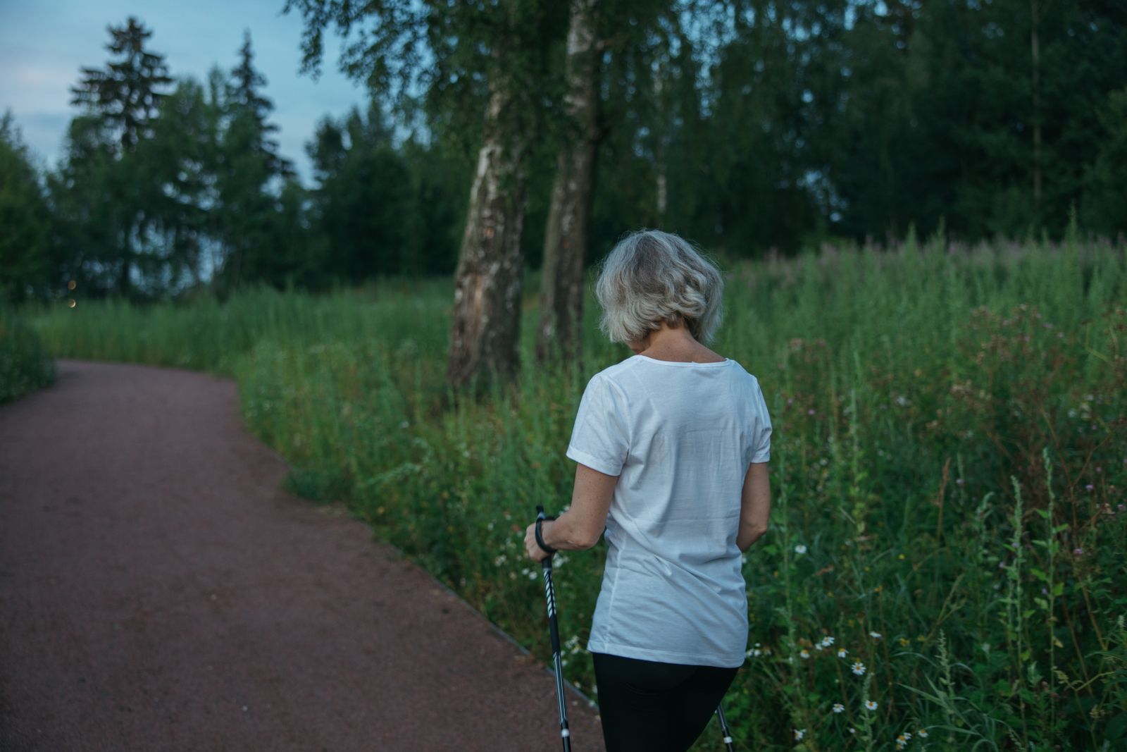 Older woman walking outdoors using a walking pole for support