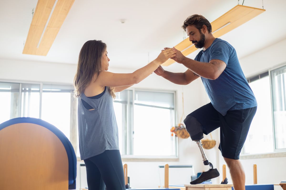 Physical therapist holding hands with a patient using a prosthetic leg during a post-surgical rehabilitation session